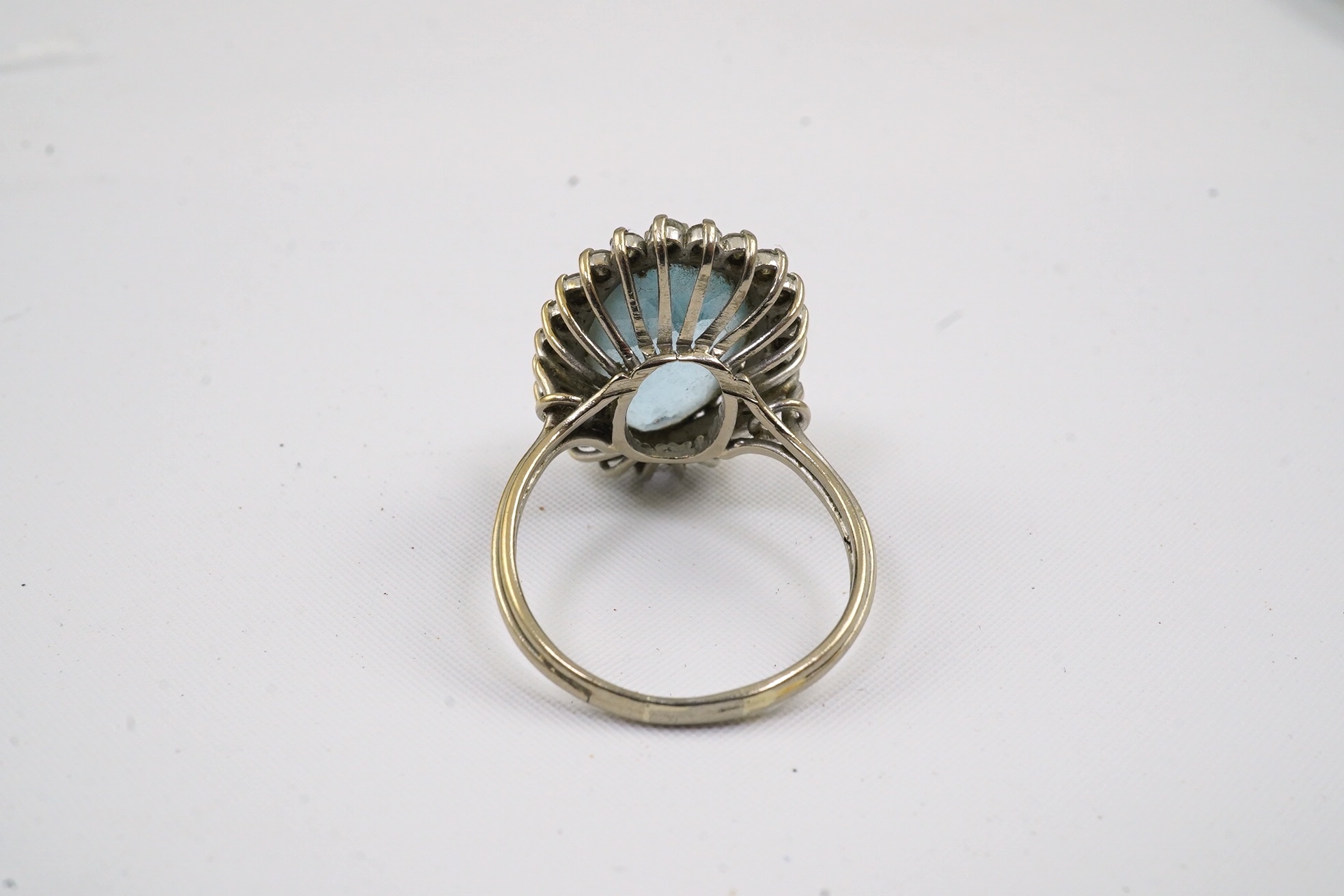 A white gold and single stone oval cut aquamarine set dress ring, with diamond cluster set border